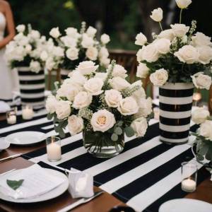 Close-up of modern white rose wedding floral arrangement in a trio of minimalist black rectangular vases on a striped tablecloth.