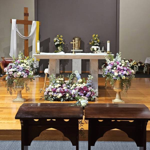Large gold urn with purple, pink, and white floral arrangement featuring eucalyptus for a church wedding.