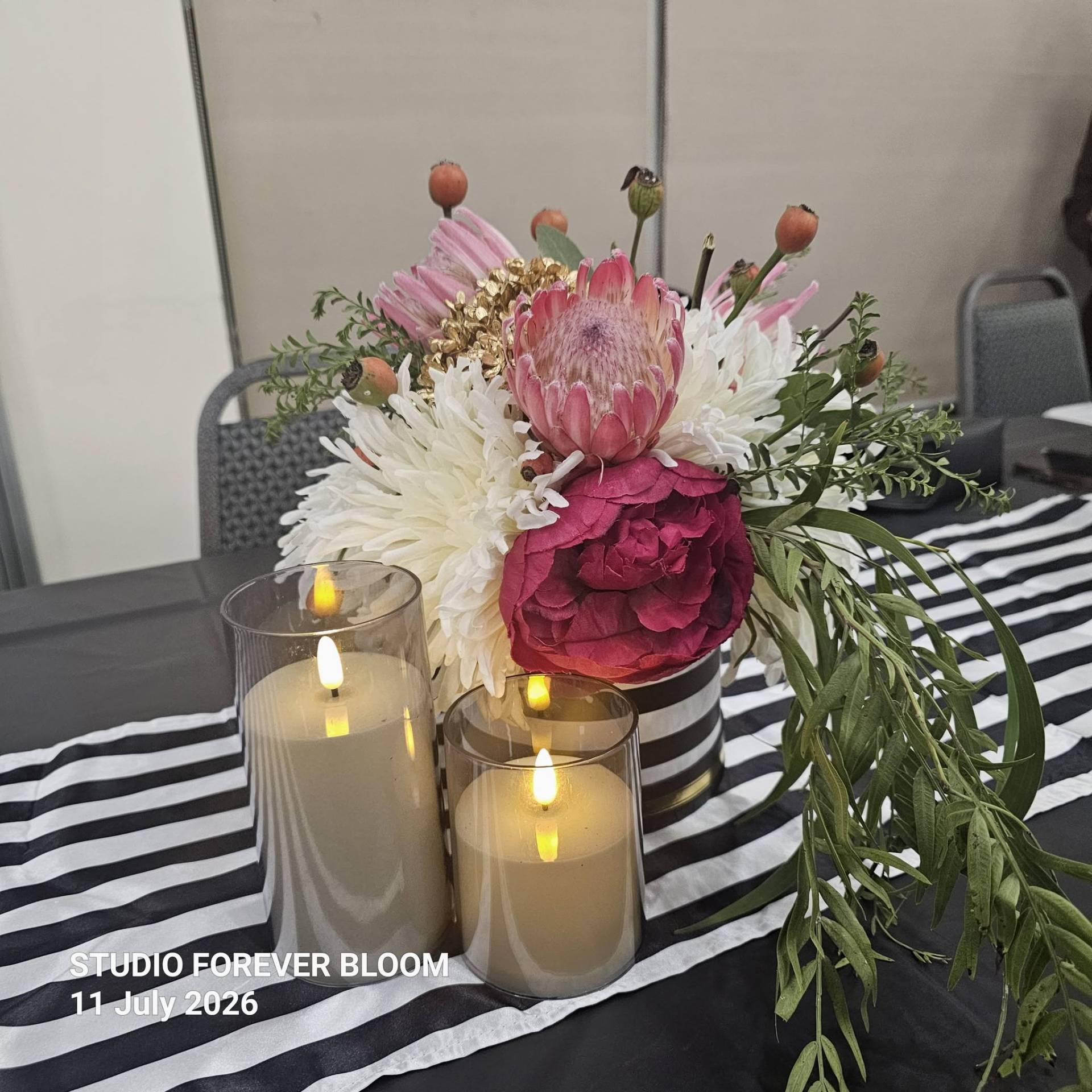 A group of four smiling elegantly dressed women standing behind a Studio Forever Bloom black and white striped hybrid floral centerpiece during an event on 11 July 2026 , Silk Floral Event Decor Melbourne