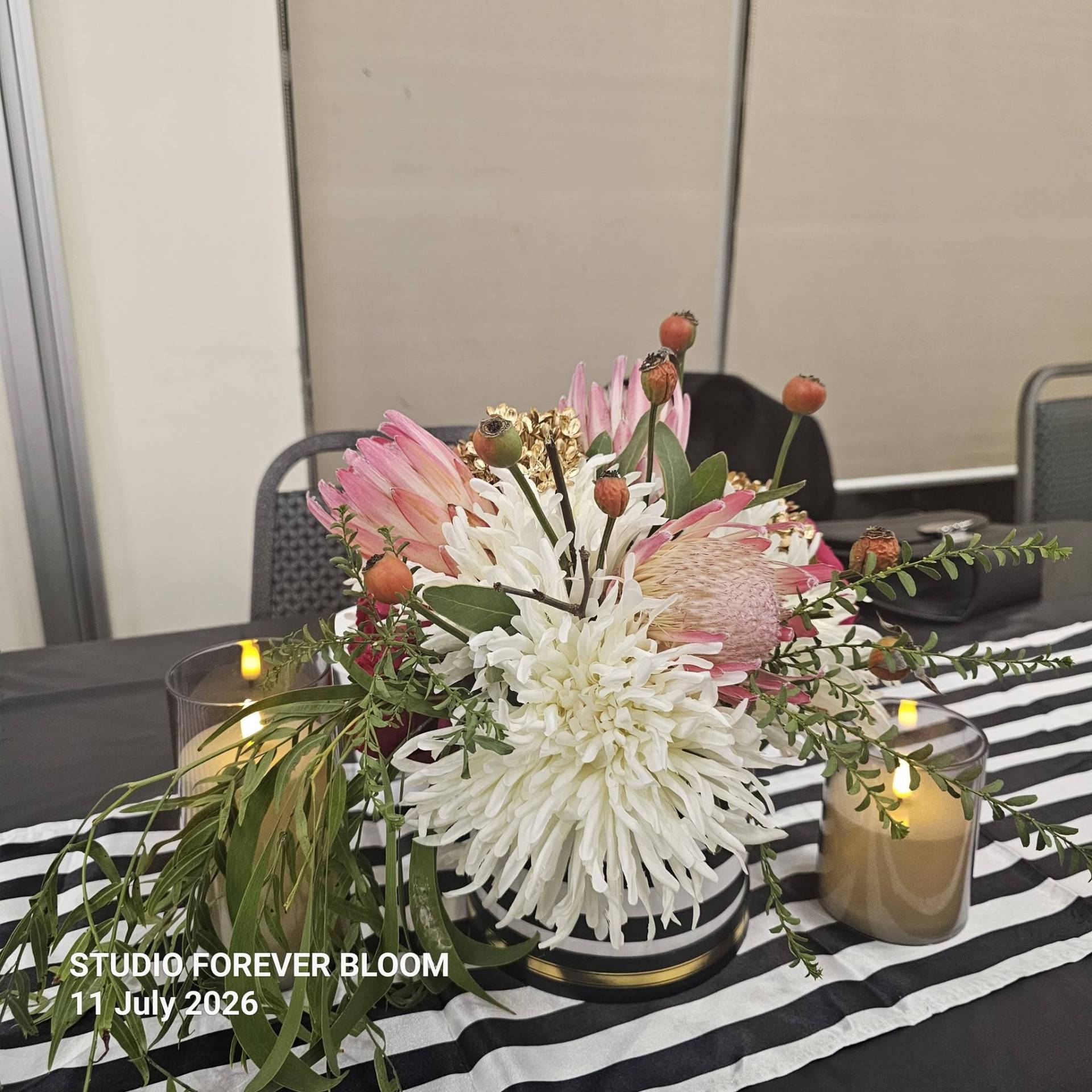 A group of four smiling elegantly dressed women standing behind a Studio Forever Bloom black and white striped hybrid floral centerpiece during an event on 11 July 2026 , Silk Floral Event Decor Melbourne