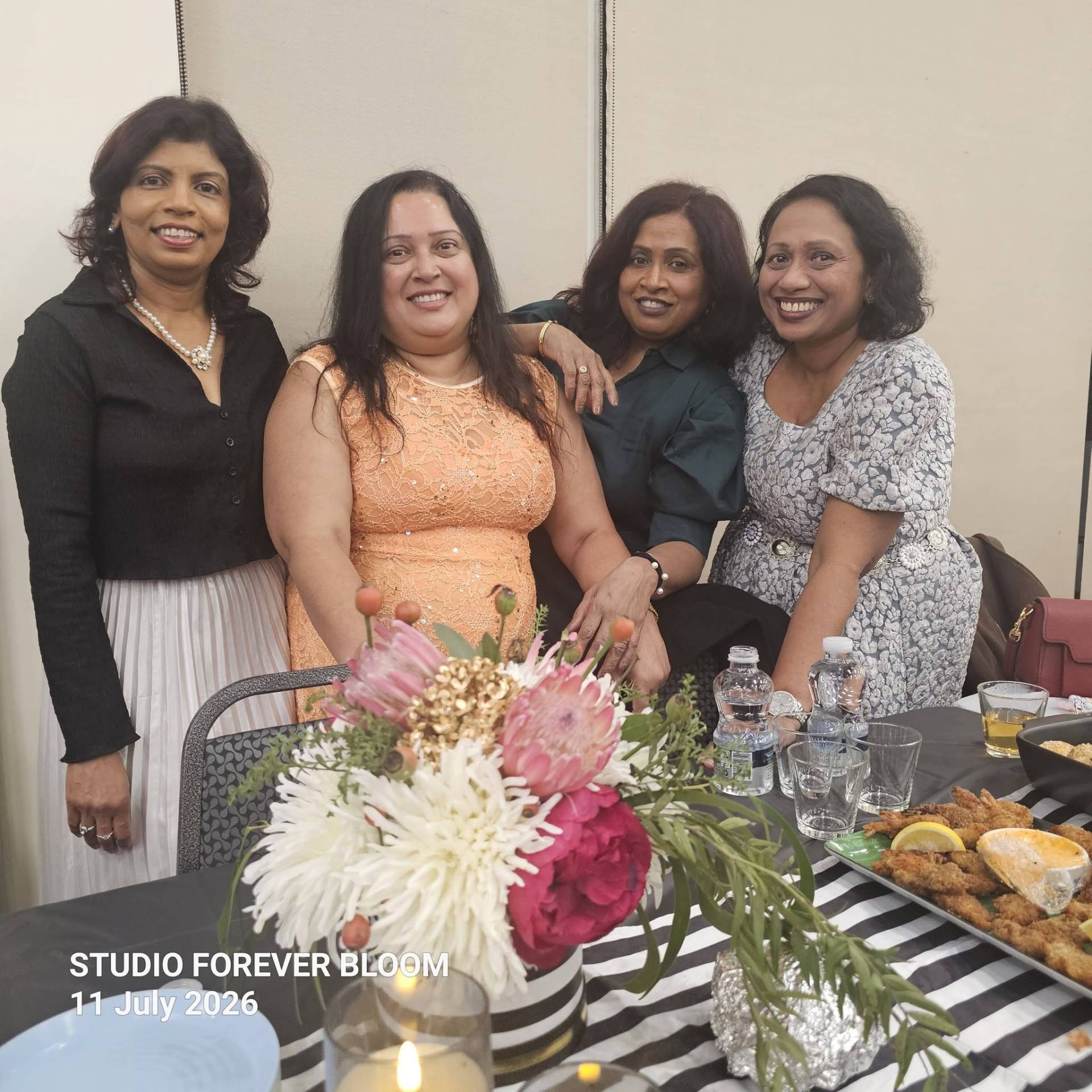 A group of four smiling elegantly dressed women standing behind a Studio Forever Bloom black and white striped hybrid floral centerpiece during an event on 11 July 2026 , Silk Floral Event Decor Melbourne
