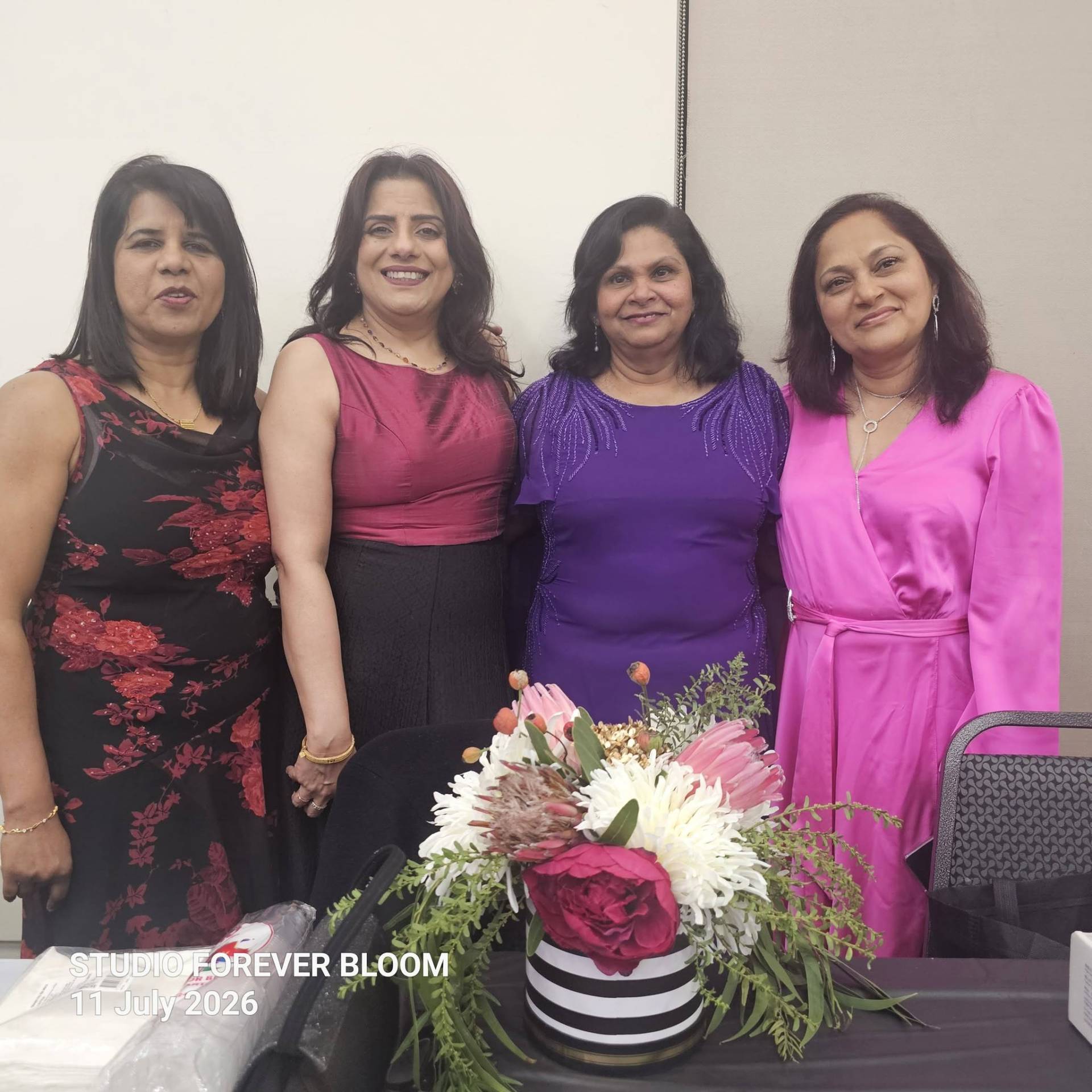 A group of four smiling elegantly dressed women standing behind a Studio Forever Bloom black and white striped hybrid floral centerpiece during an event on 11 July 2026 , Silk Floral Event Decor Melbourne