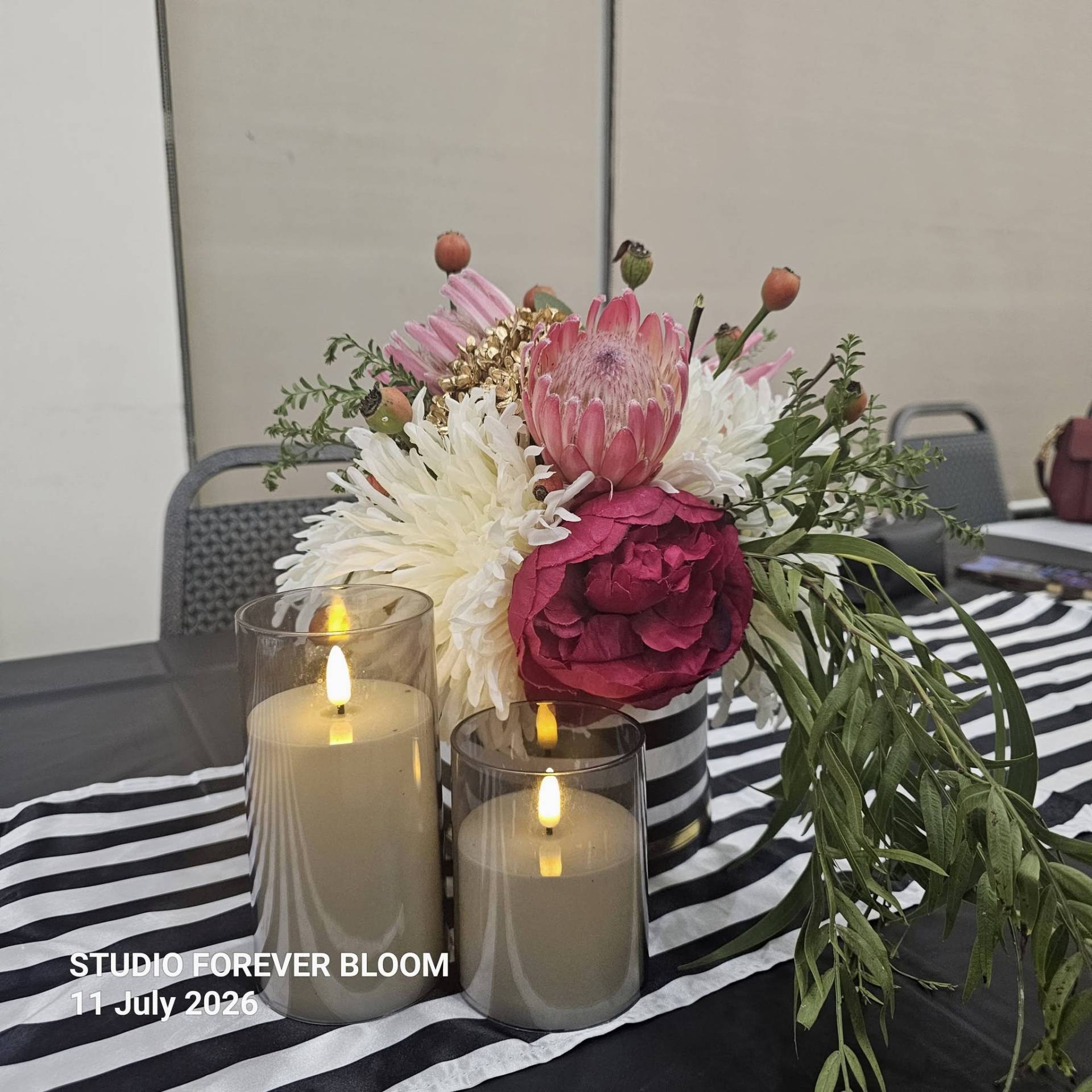 A group of four smiling elegantly dressed women standing behind a Studio Forever Bloom black and white striped hybrid floral centerpiece during an event on 11 July 2026 , Silk Floral Event Decor Melbourne