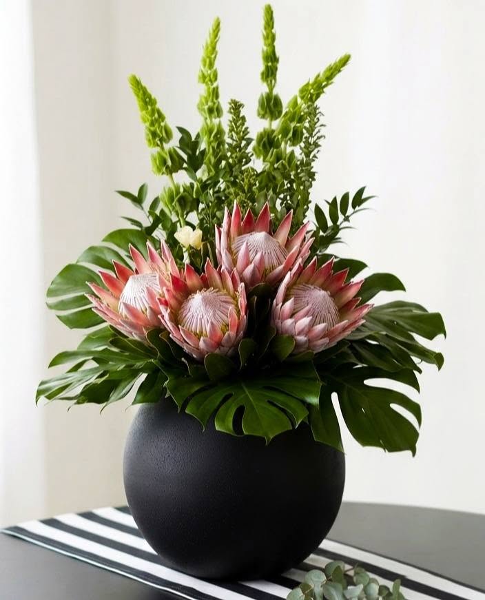 A luxury living room featuring the Elegant Protea Arrangement in a black pot on a side table next to a black textured abstract painting on an easel Protea Floral Decor Melbourne