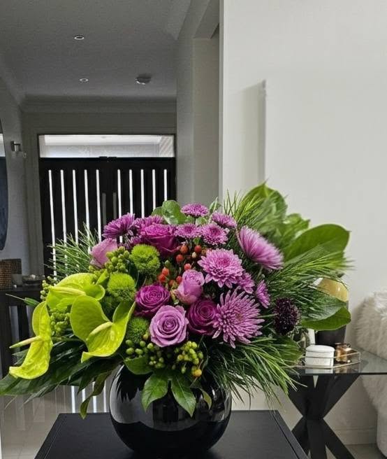A luxury event decor showcase by Studio Forever Bloom featuring a tall purple and green hybrid floral pillar next to matching silk centerpieces in black pots.
