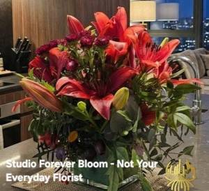 A luxury winter-themed floral display named WINTER LILIES Red Hybrid Arrangement V1 featuring large red lilies, dark burgundy blooms, and eucalyptus by Studio Forever Bloom.