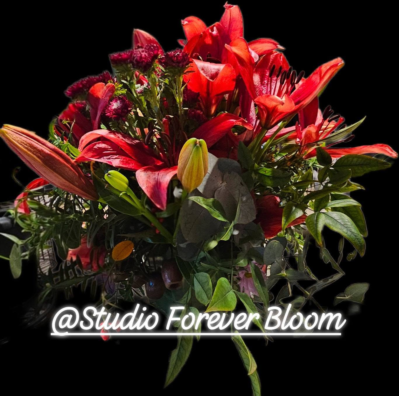 A luxury winter-themed floral display named WINTER LILIES Red Hybrid Arrangement V1 featuring large red lilies, dark burgundy blooms, and eucalyptus by Studio Forever Bloom.